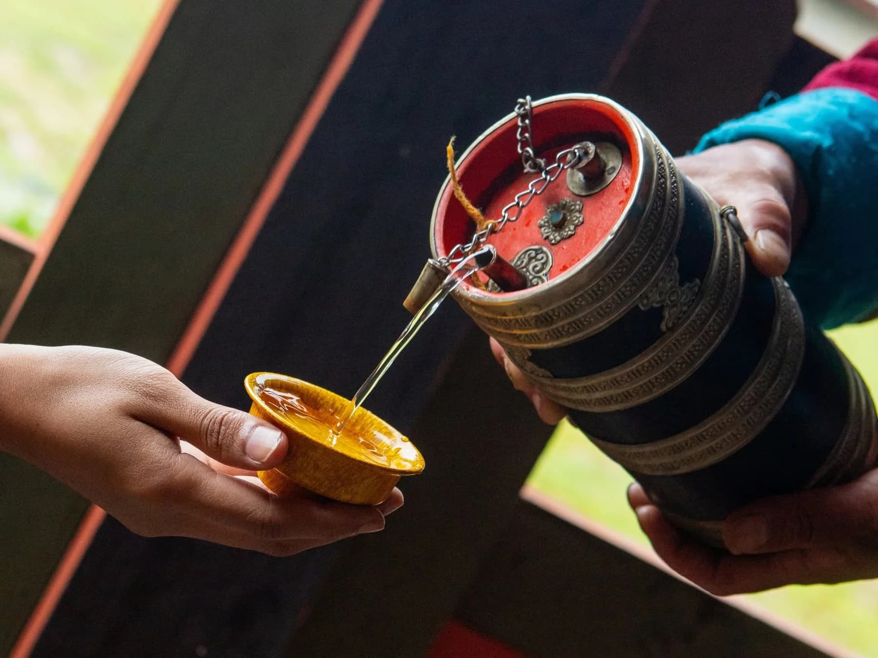 Hands pouring tea from a traditional vessel into a small bowl