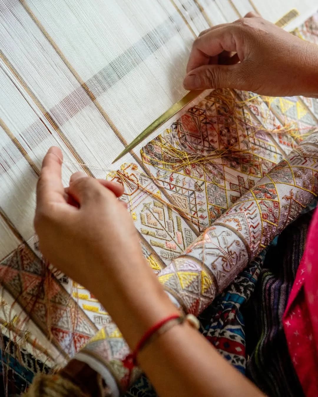 Close-up of hands guiding thread on a loom with a woven pattern
