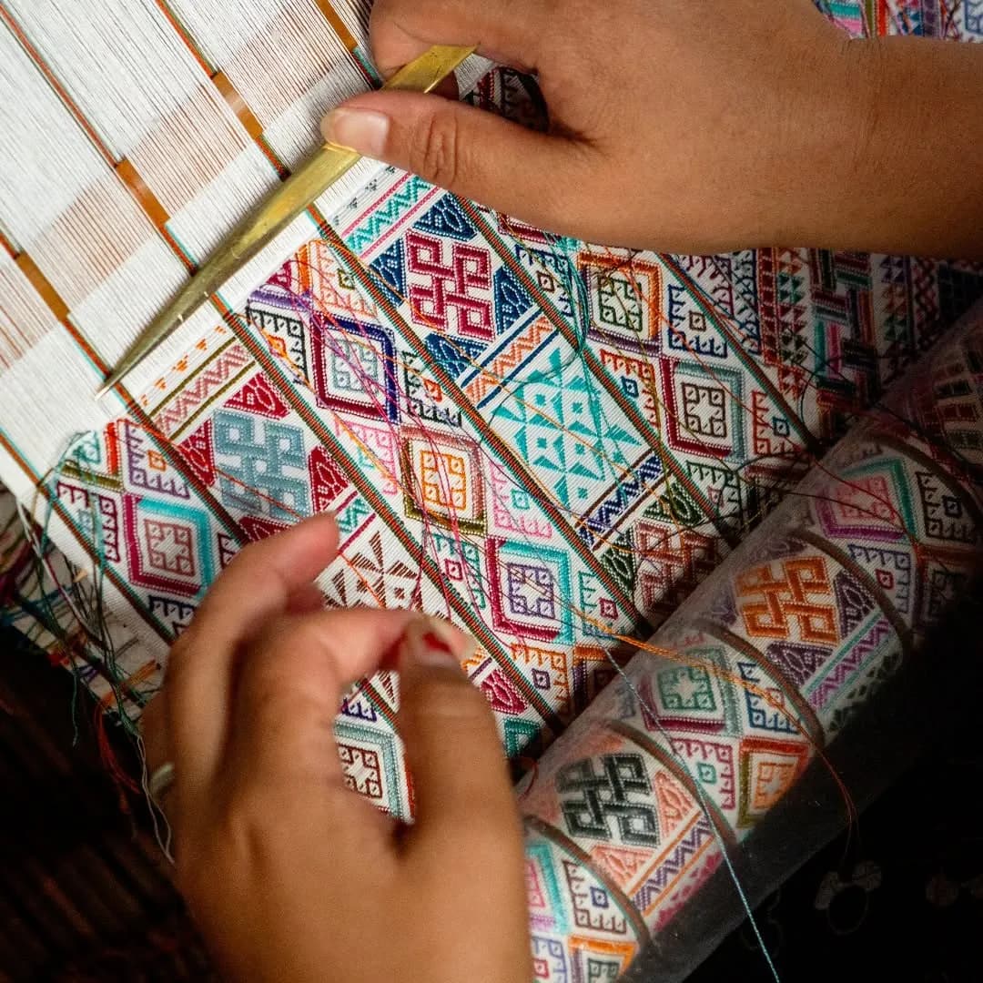 Hands weaving a brightly coloured Bhutanese textile on a loom