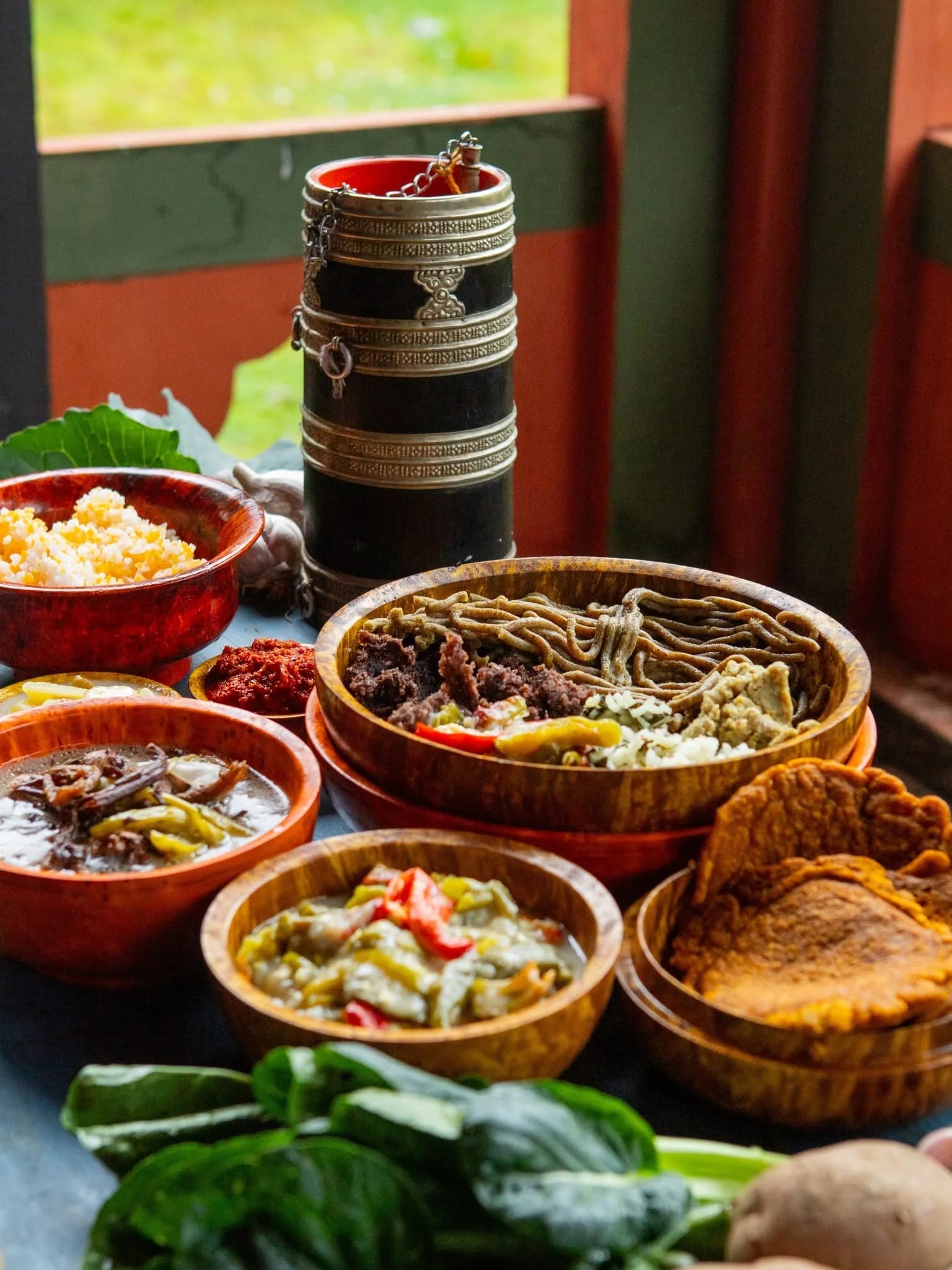 A table of home-style Bhutanese food in wooden bowls by a window