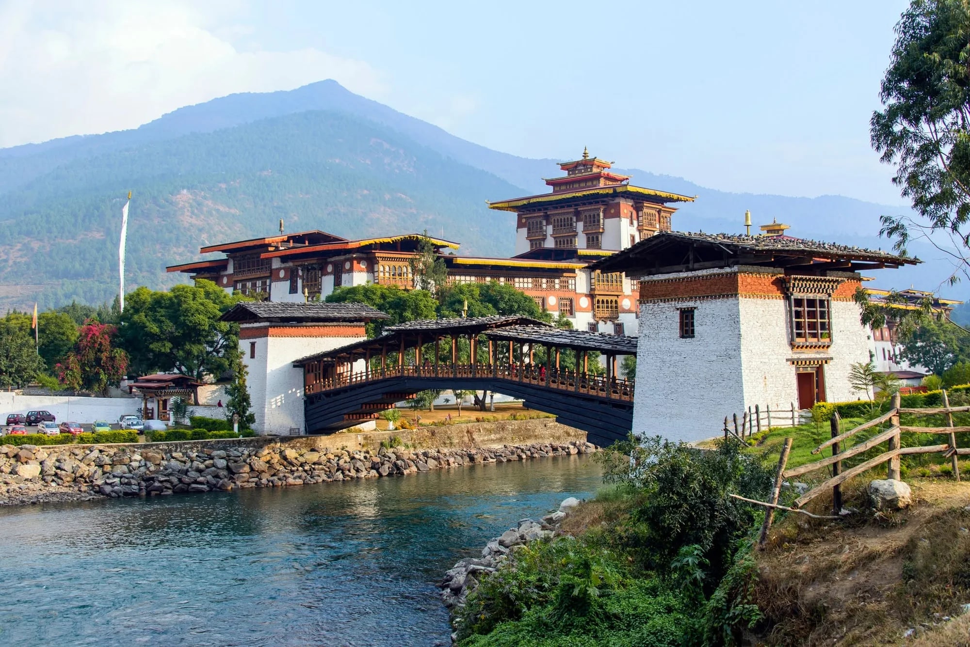A traditional Bhutanese fortress by a river with a wooden bridge